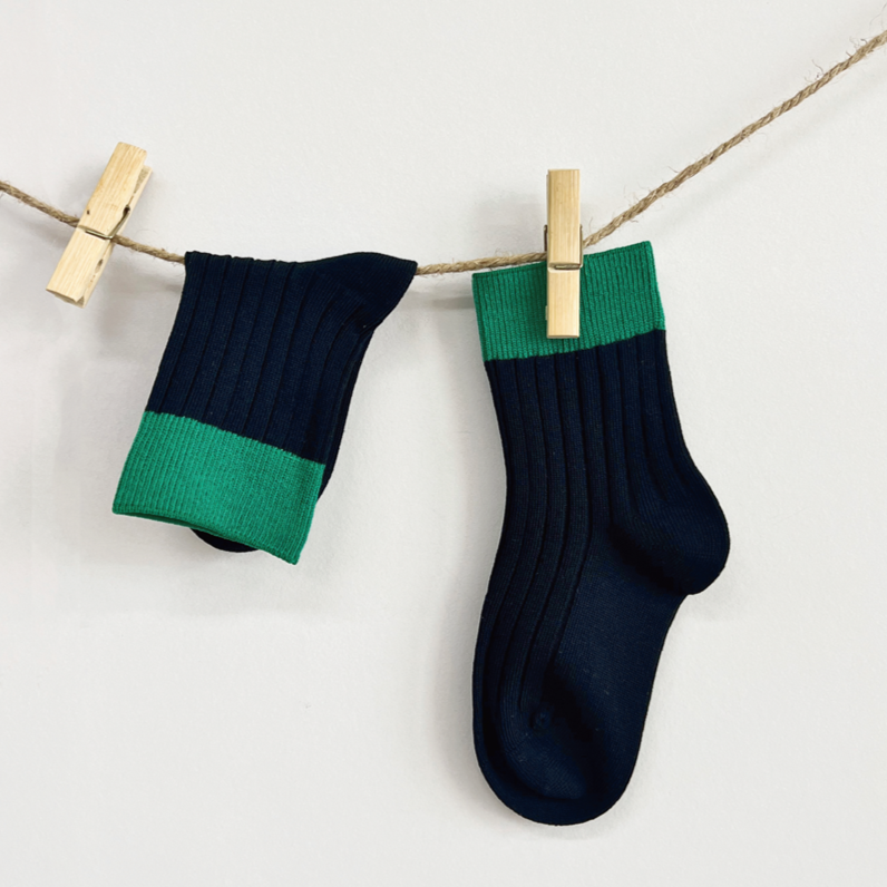Navy and green socks hanging on a clothesline with wooden clips against a white background