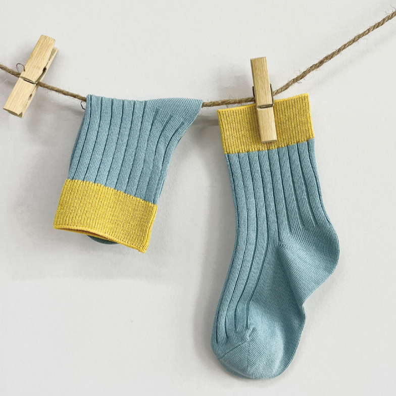 Pair of blue socks with yellow trim hanging on a line with wooden clips.