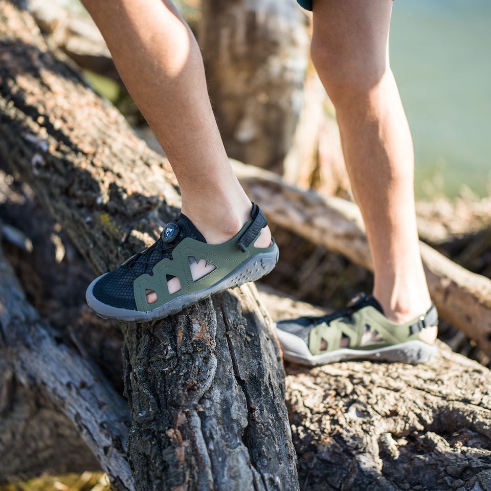 A kid wearing green and black sandals standing on a log with a natural background