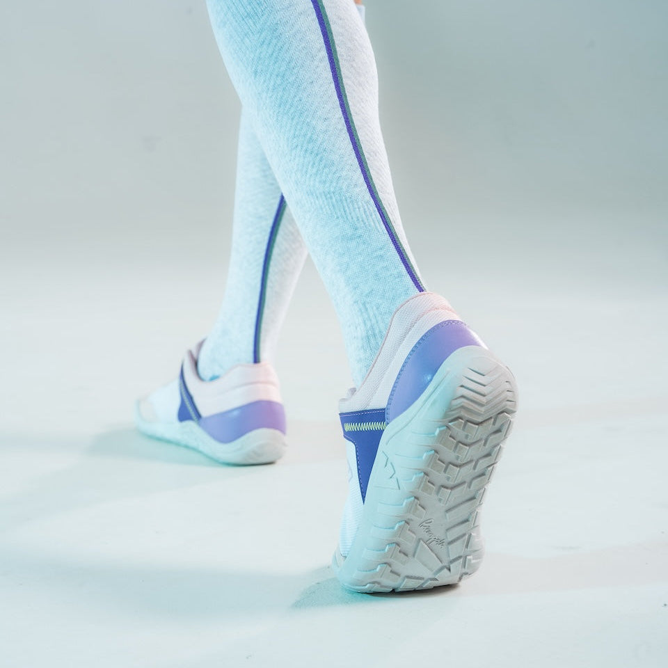 White sneakers with blue accents worn with light blue knee-high socks on a light gray background